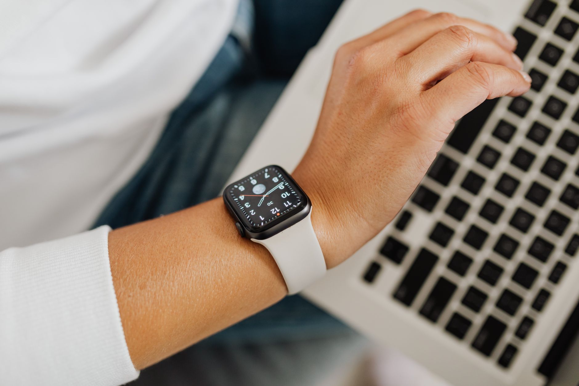 Person checking health metrics on a smartwatch while using a laptop in a bright workspace